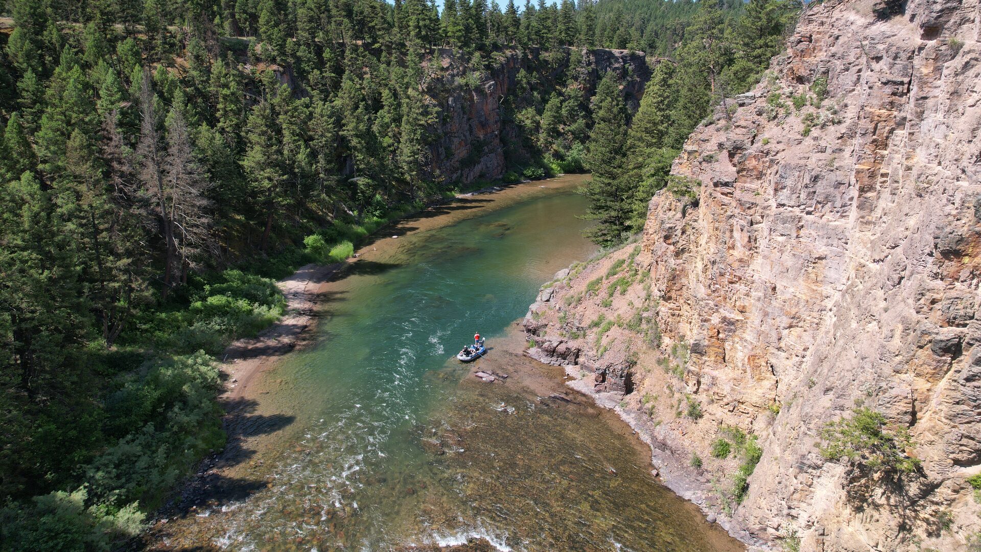 A raft on green water beneath a sheer cliff on the Blackfoot