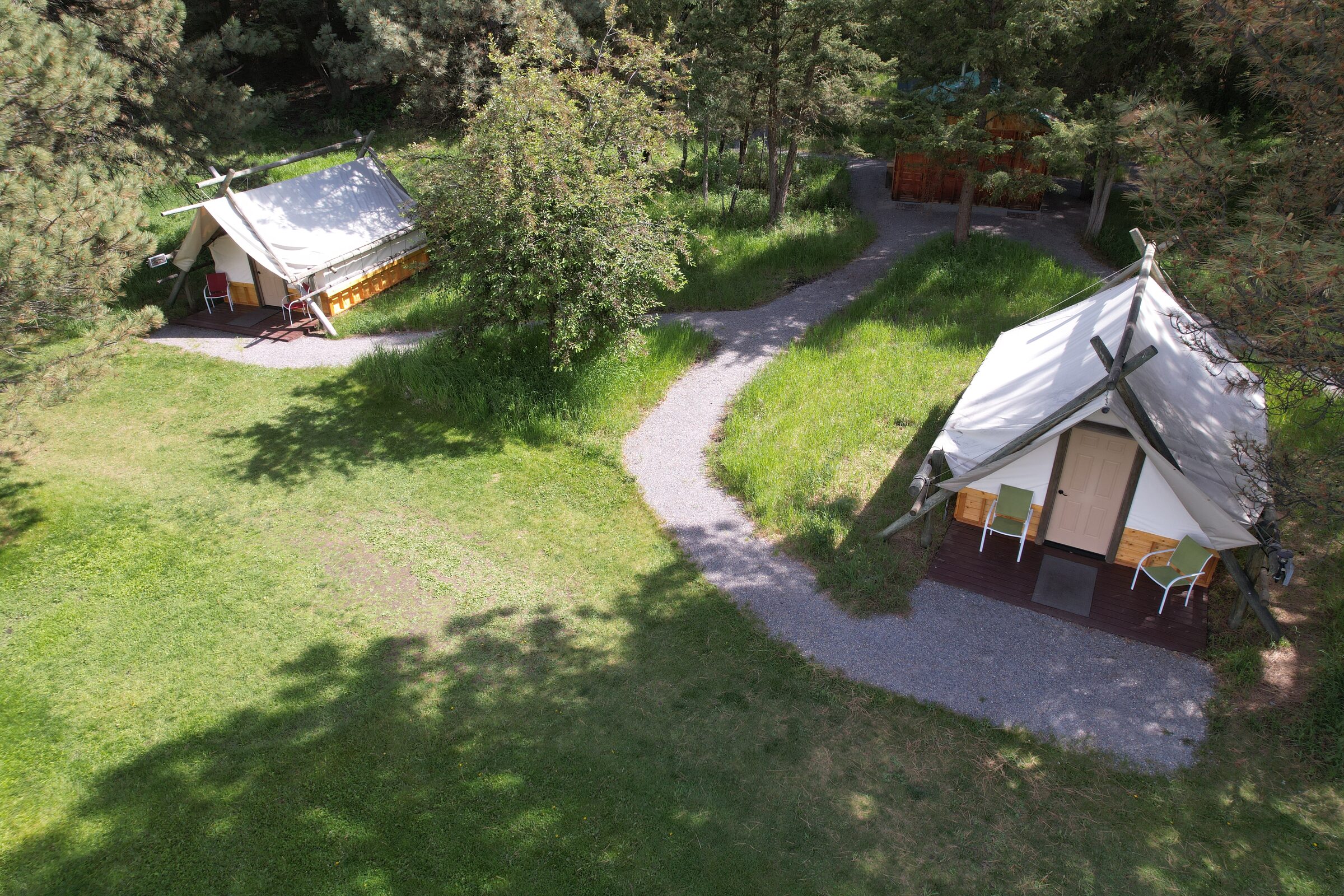 Two tent cabins joined by a gravel path through the grass