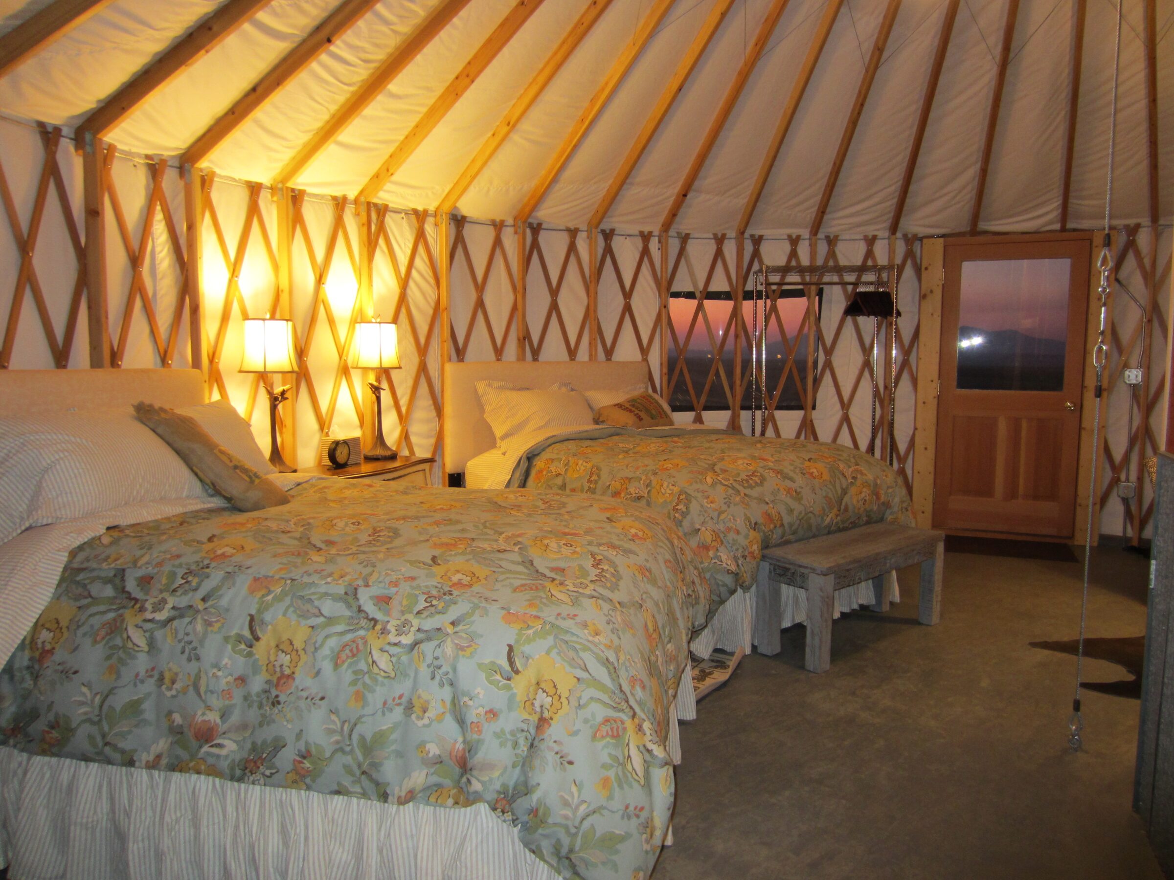 A guest yurt at sunset, its two beds lit by bedside lamps