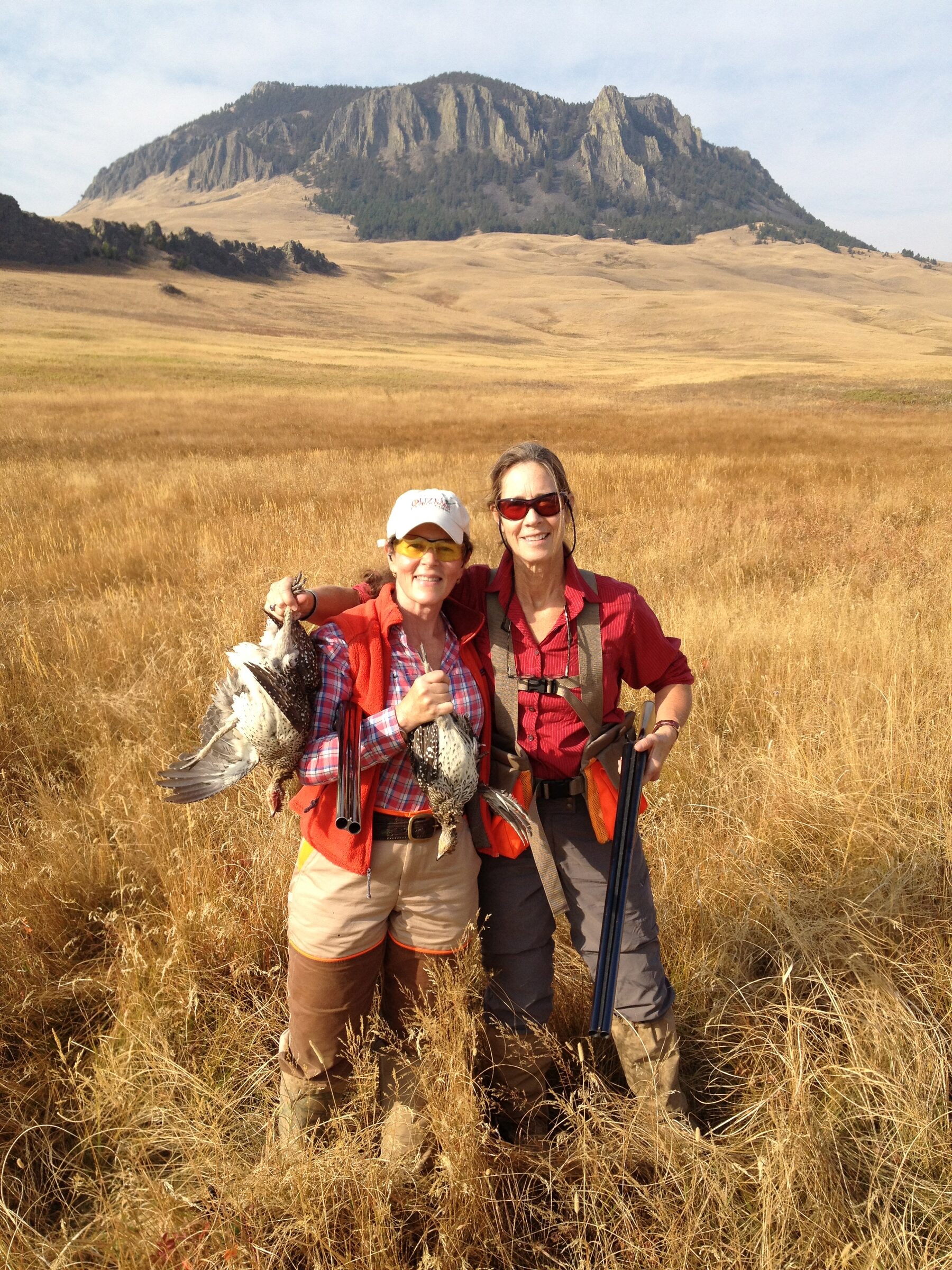 Two hunters with their birds, a flat-topped butte behind them