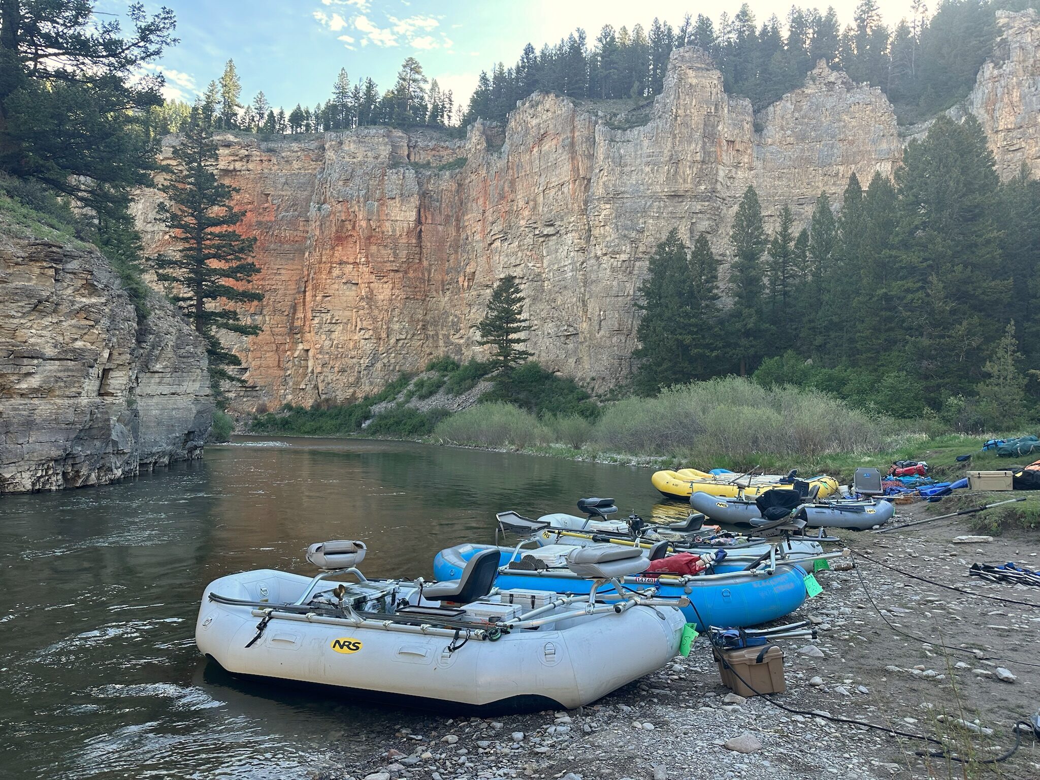 Rafts pulled up on the gravel below a sheer canyon wall