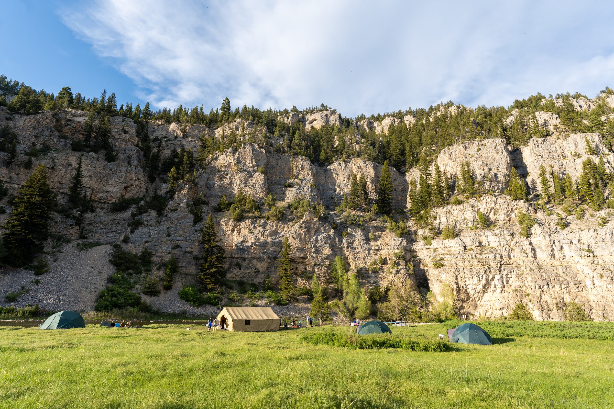 Tents pitched in a riverside meadow under the limestone walls